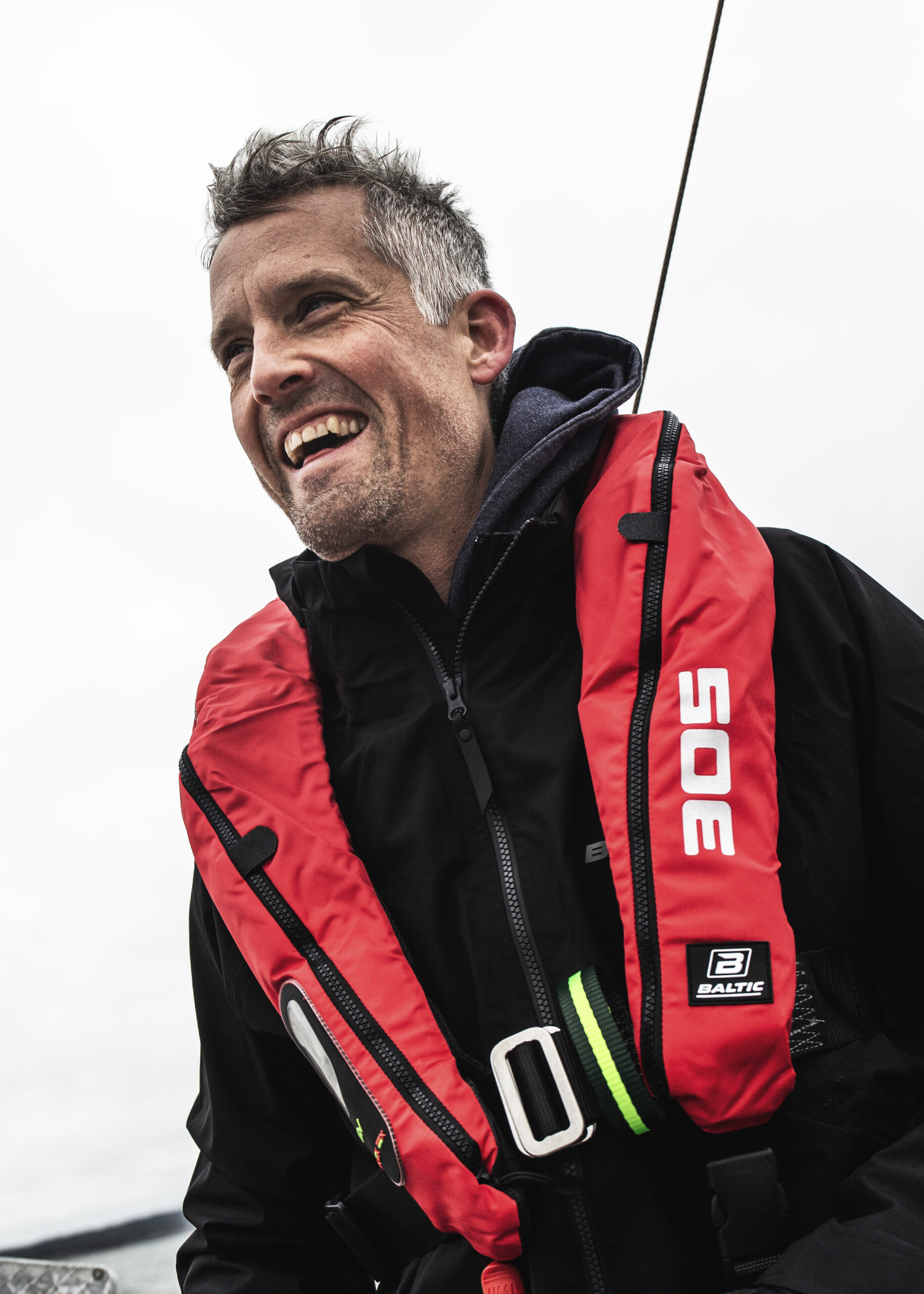 En man står med en röd flytväst och ler stort.